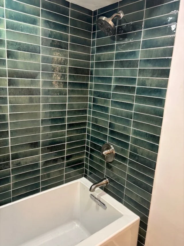 Bathroom shower with dark green tiles, a showerhead, a faucet, and a white bathtub.