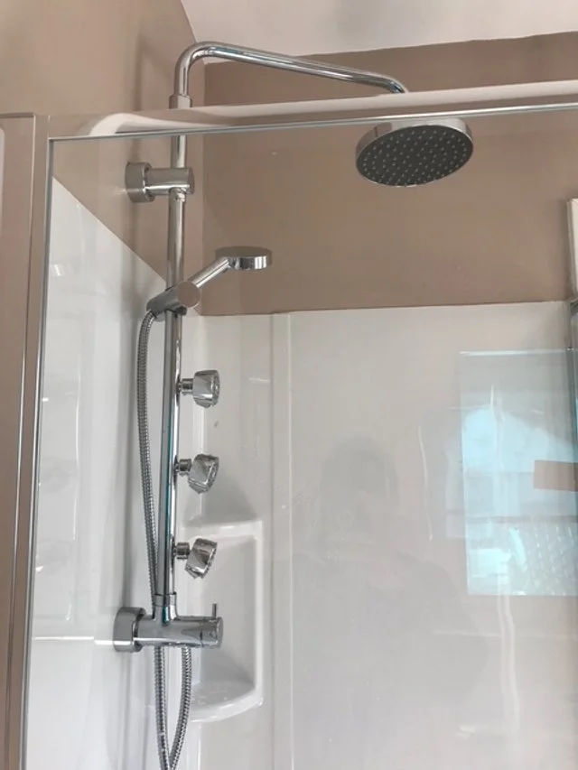 A modern shower with multiple adjustable body sprays, a handheld showerhead, and a rainfall showerhead in a glass enclosure.