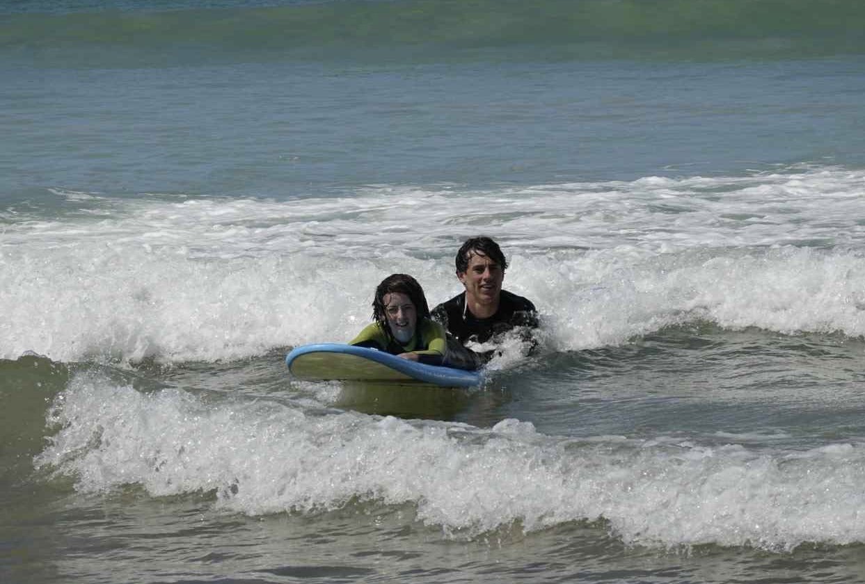 Two people riding a boogie board in the ocean surf with small waves.