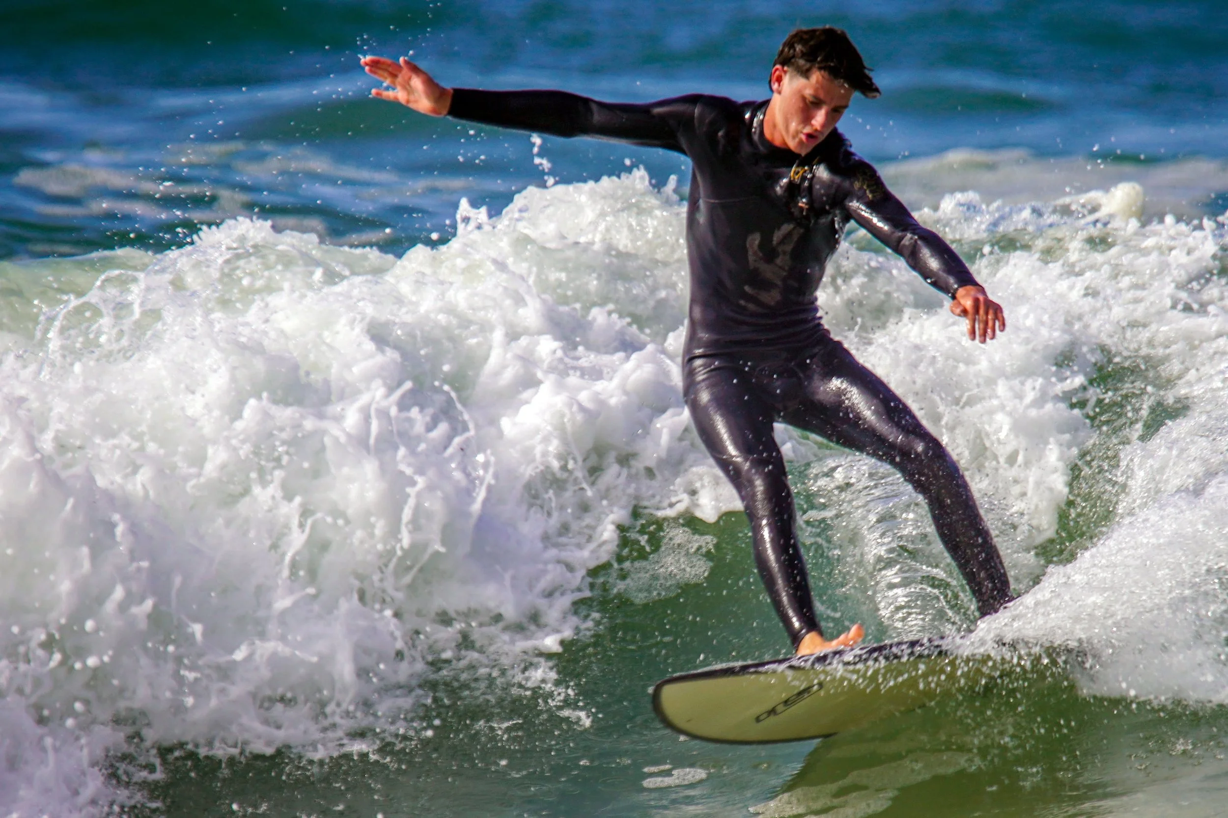 A person wearing a wetsuit riding a surfboard on a wave at the beach.