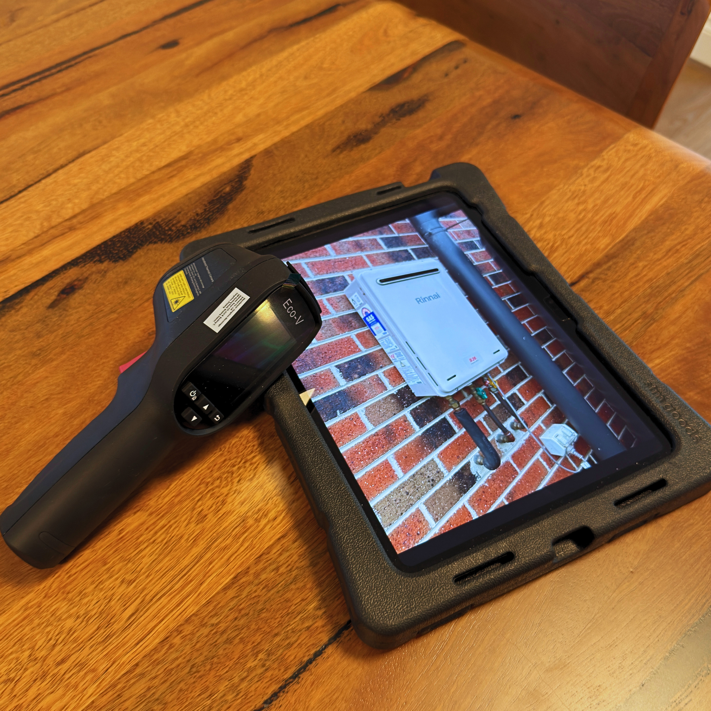 A wooden table with a black electronic device and a white tablet displaying a brick wall background.