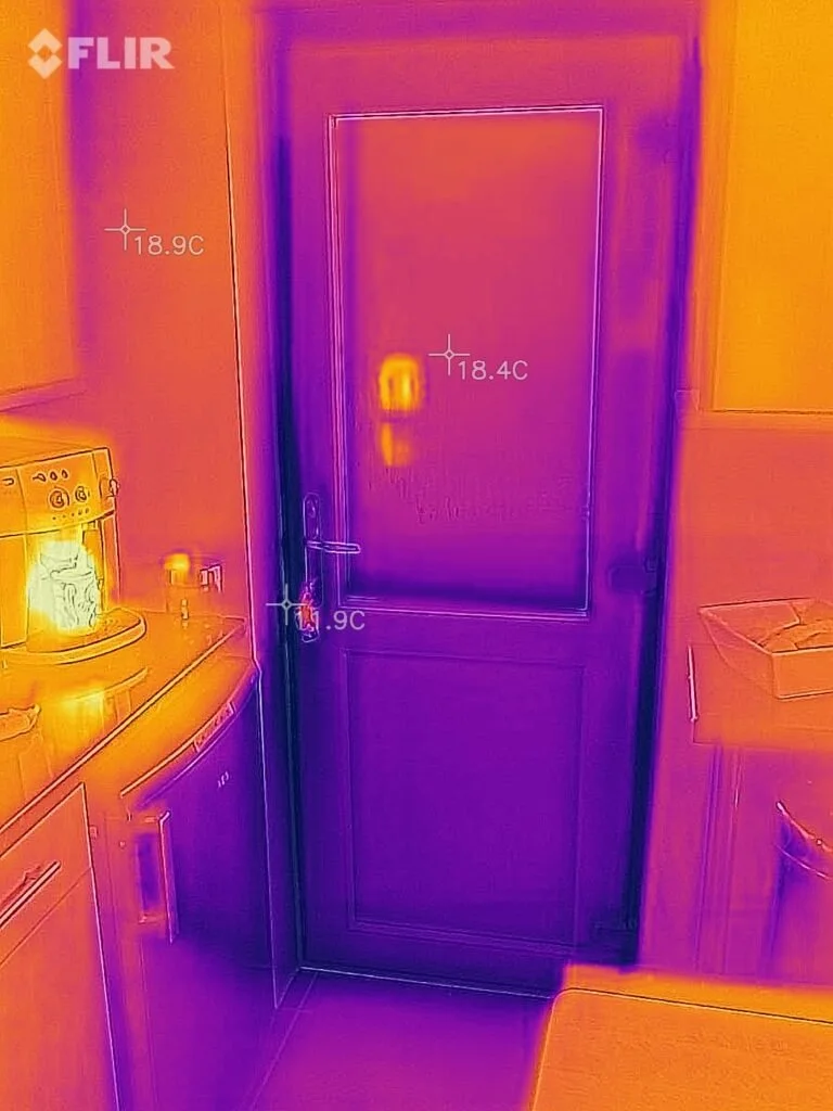 Thermal image of a closed door in a room, showing temperature variations on the surface, with cooler areas in purple and warmer areas in yellow, orange, and red.