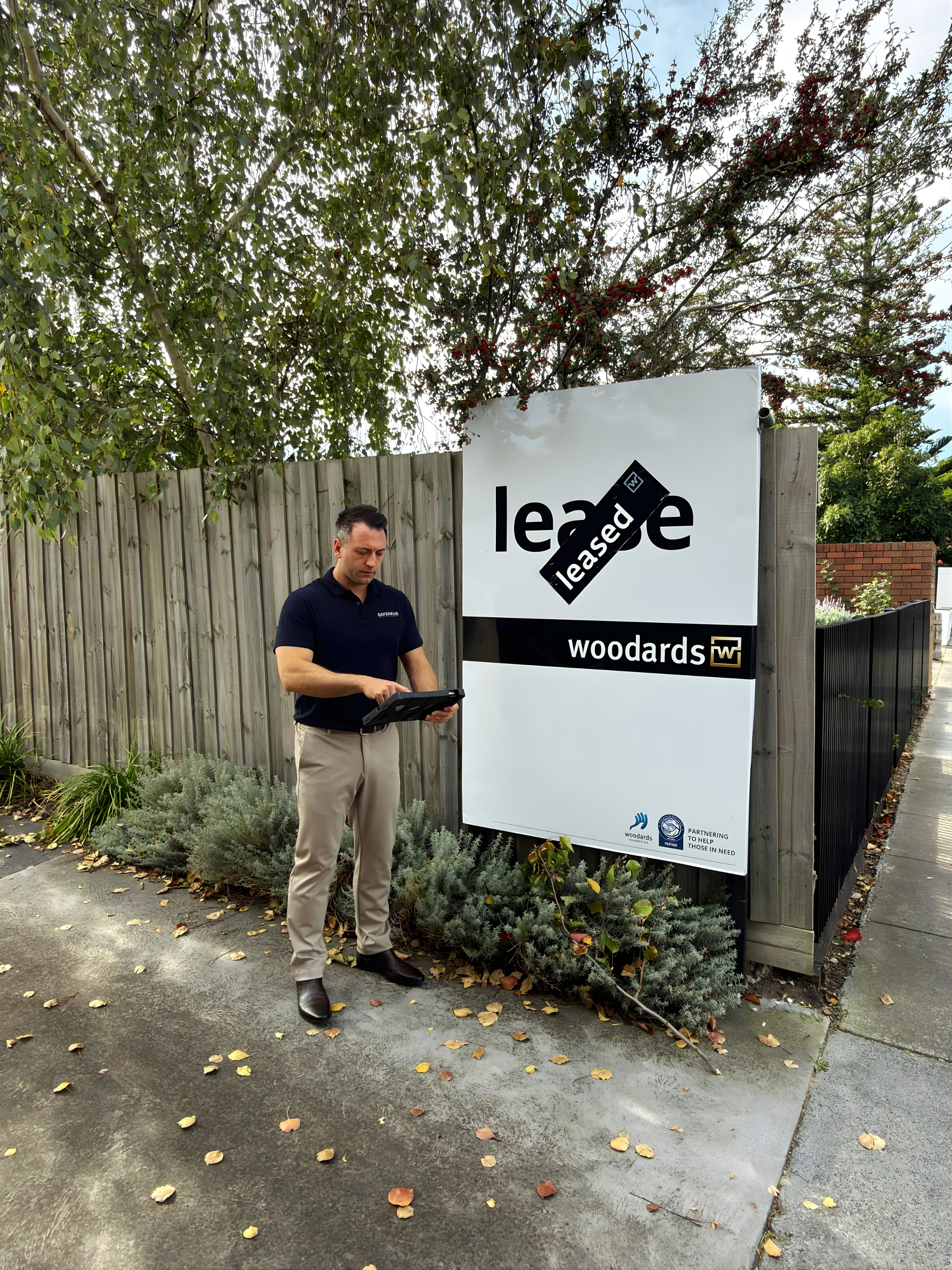 Man standing on sidewalk, looking at a device, behind a large sign that reads 'lease' with
