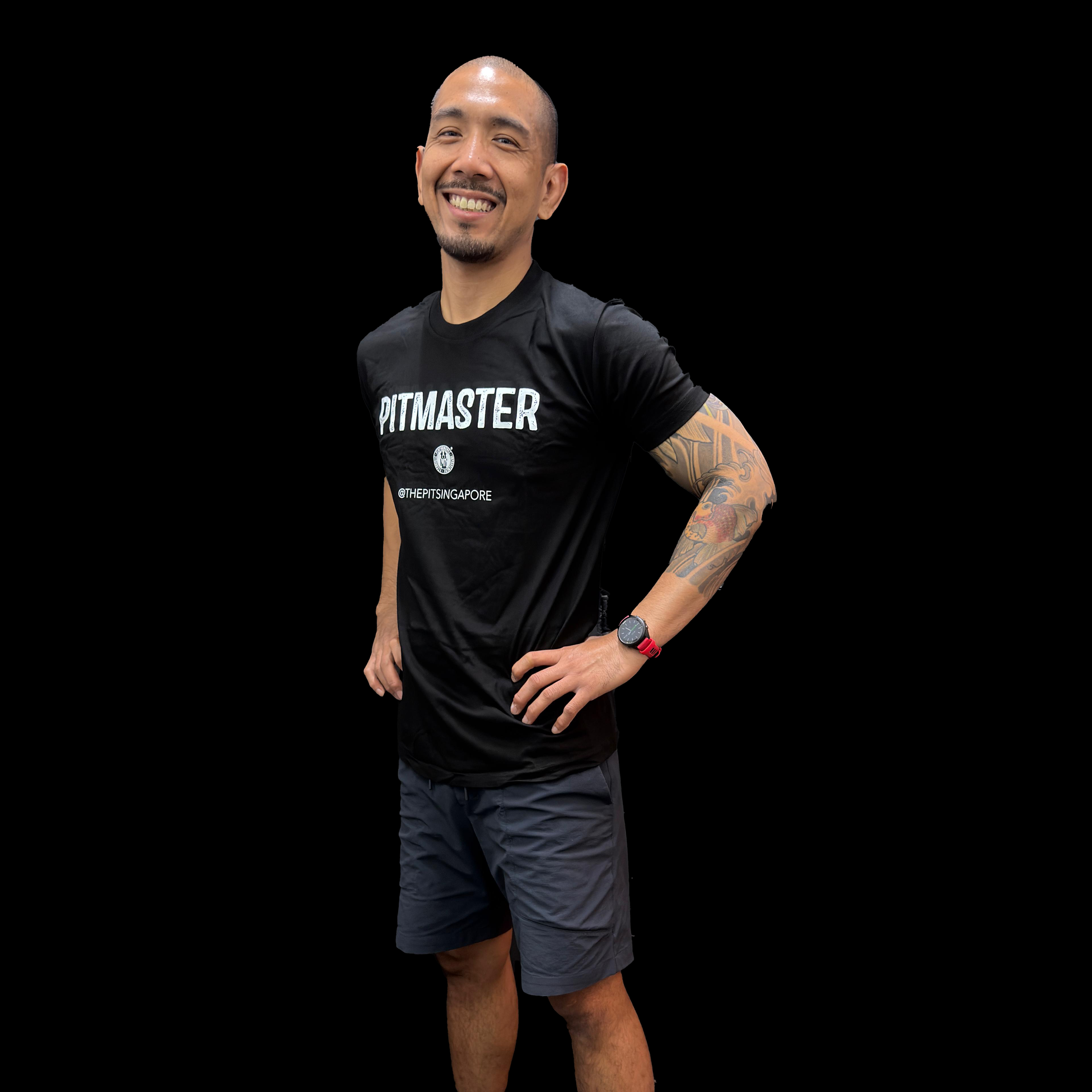 Smiling man in athletic black t-shirt and shorts standing with hands on hips against a black background.