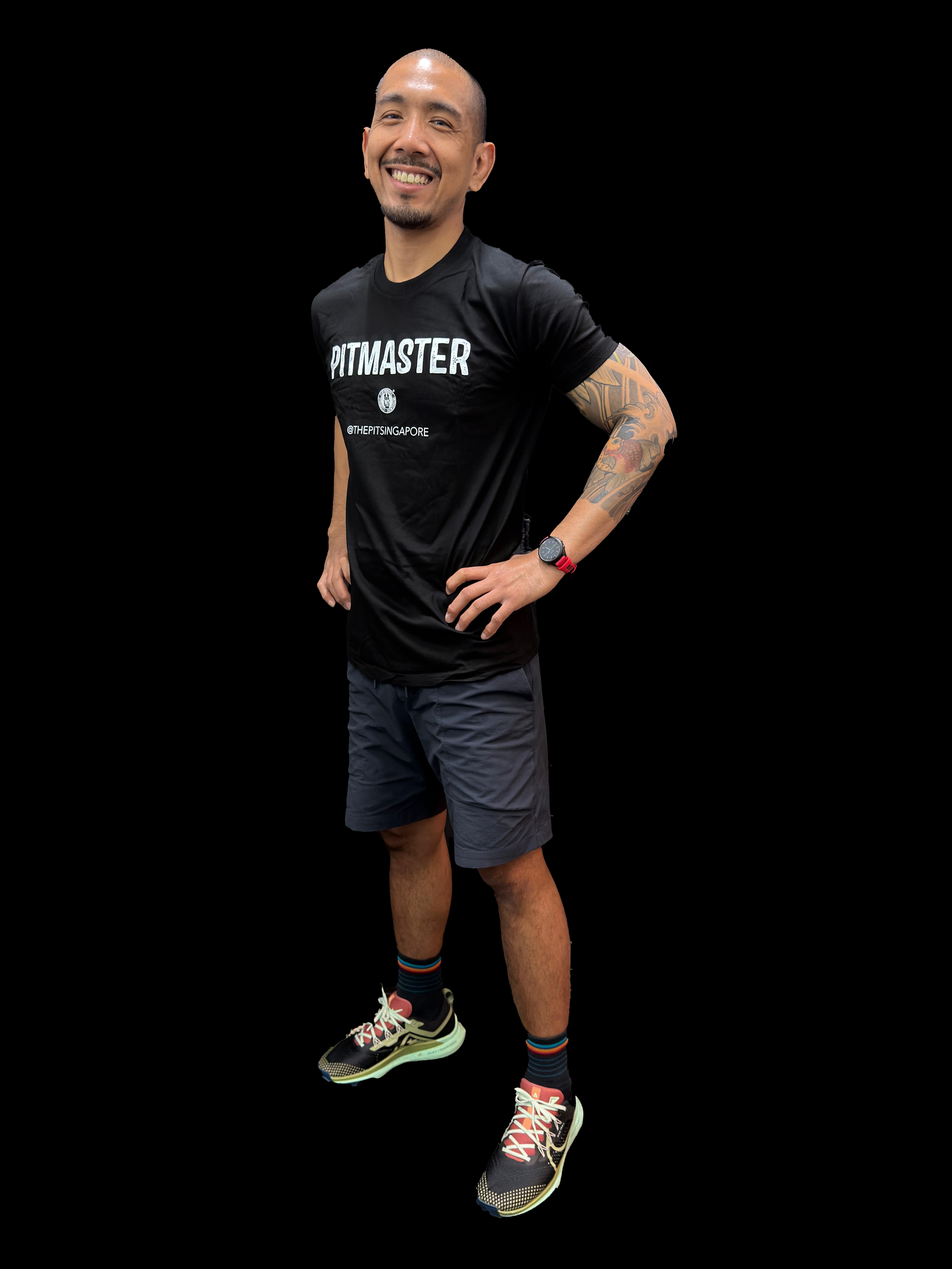 A smiling man in athletic attire stands with hands on hips, wearing a black T-shirt, shorts, colorful socks, running shoes, and a watch.