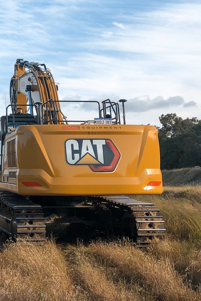 A yellow Caterpillar excavator with tracked wheels parked on a grassy field under a partly cloudy sky.