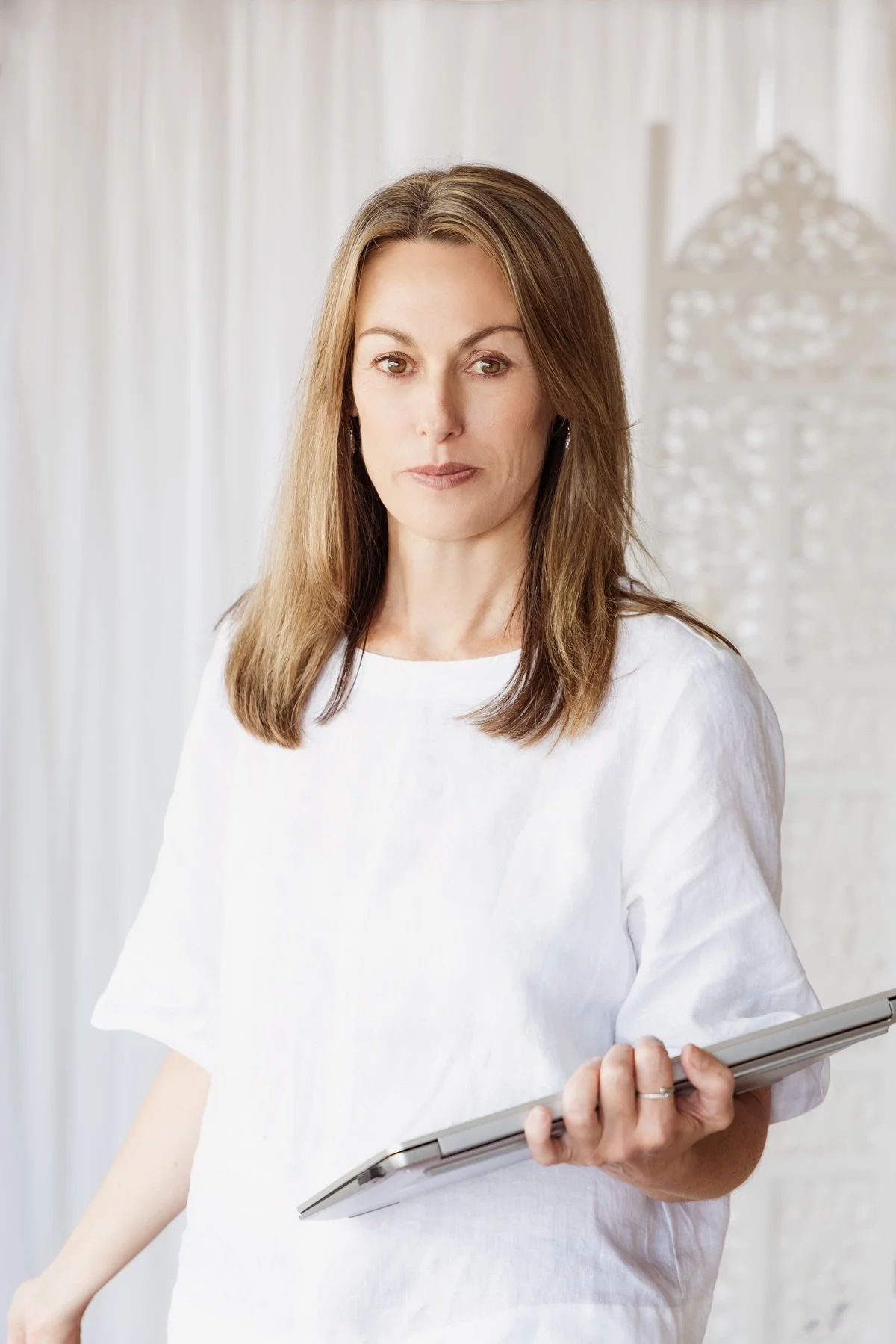 Lisa Proctor, town planner and environmental consultant, brown hair, white shirt, holding laptop, white curtain background.
