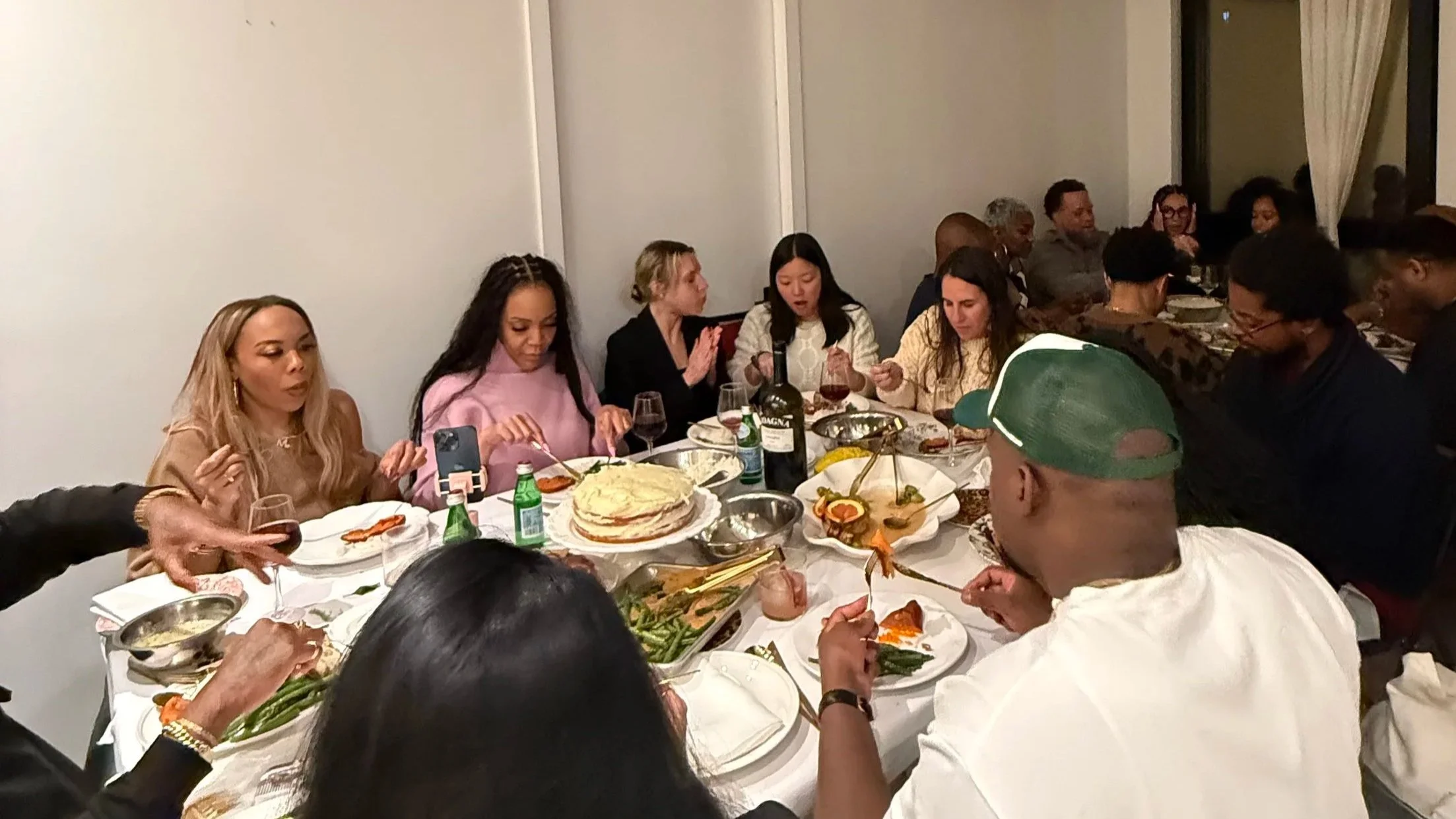 A group of people dining at a dinner party with food and wine on a table.