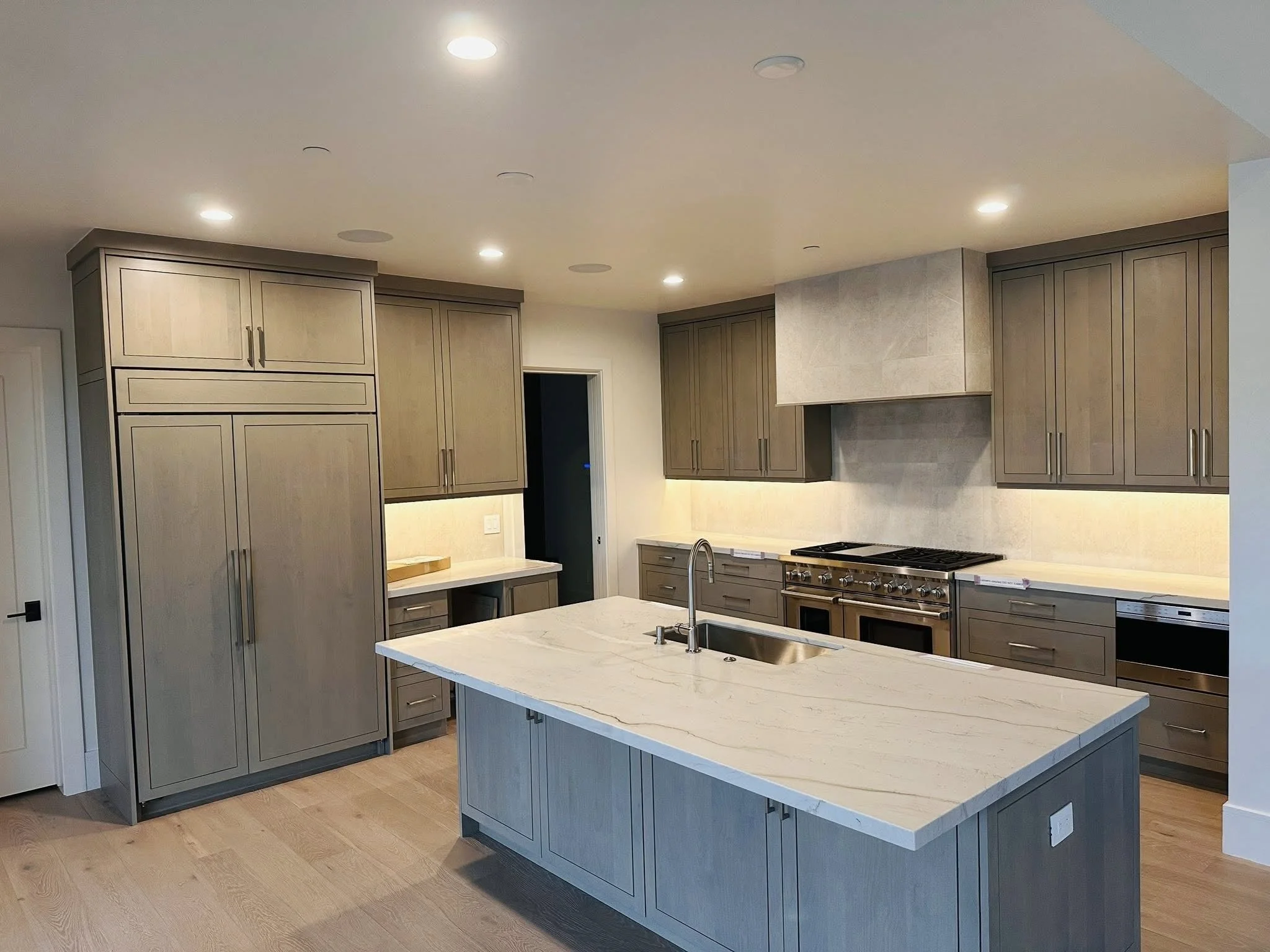 Modern kitchen with beige cabinets, stainless steel appliances, an island with a marble countertop, and recessed lighting.