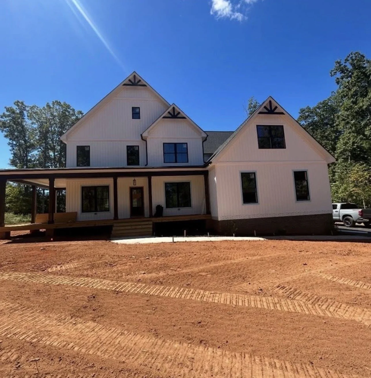 Newly constructed white house with black trim, multiple gable roofs, a front porch, and a dirt yard under a clear blue sky.