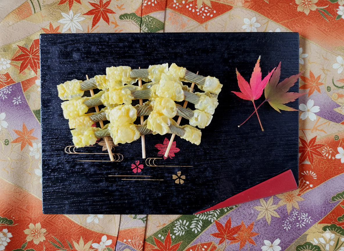 四角い黒い皿の上に小菊巻が置かれている。背景は紅葉柄の伝統的な模様の布。
