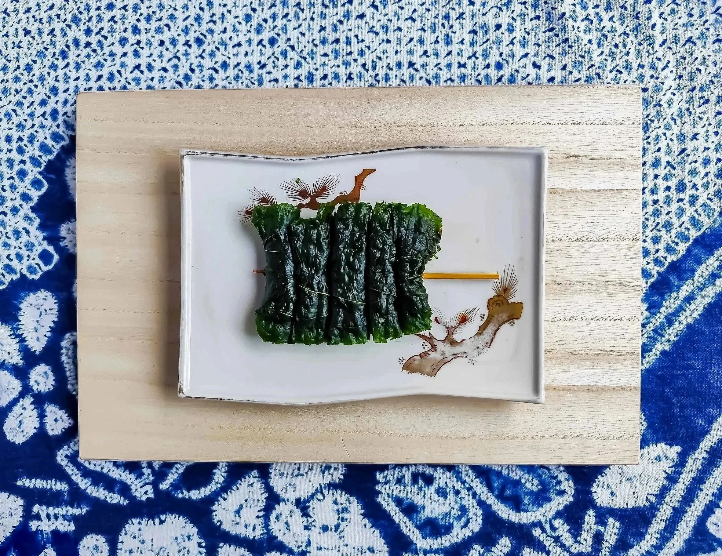 海苔巻きのもみじ柄の皿の上に、海苔に包まれた料理が置かれている。背景は青と白の伝統的な模様の布。