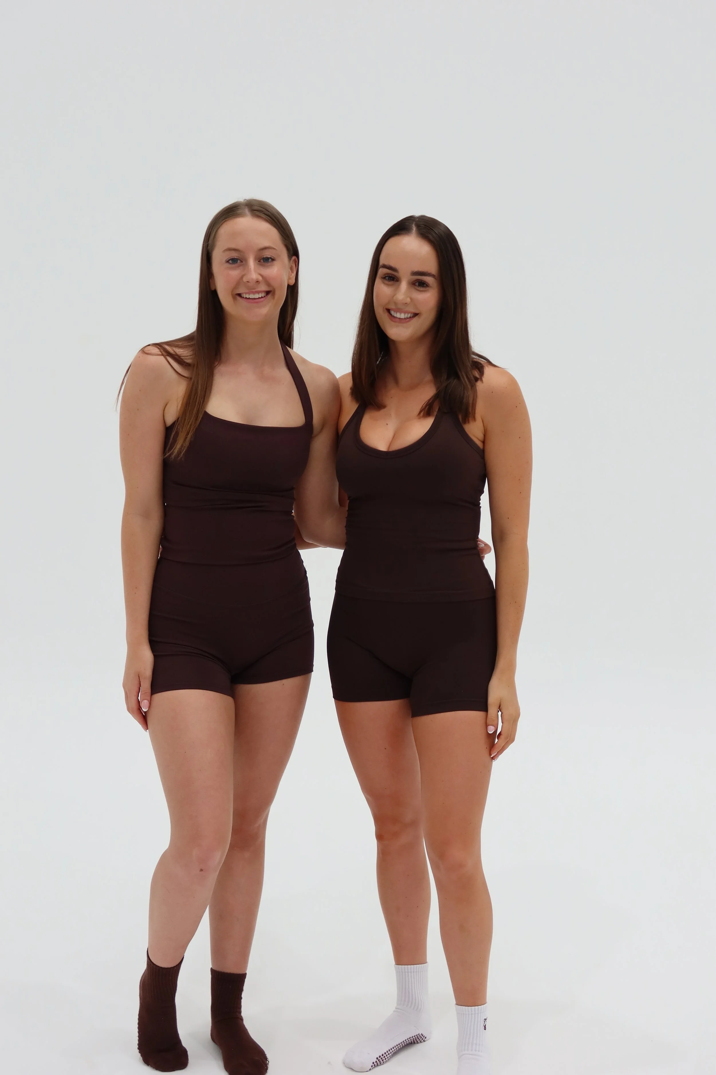 Two young women standing together in black athletic outfits against a plain background.