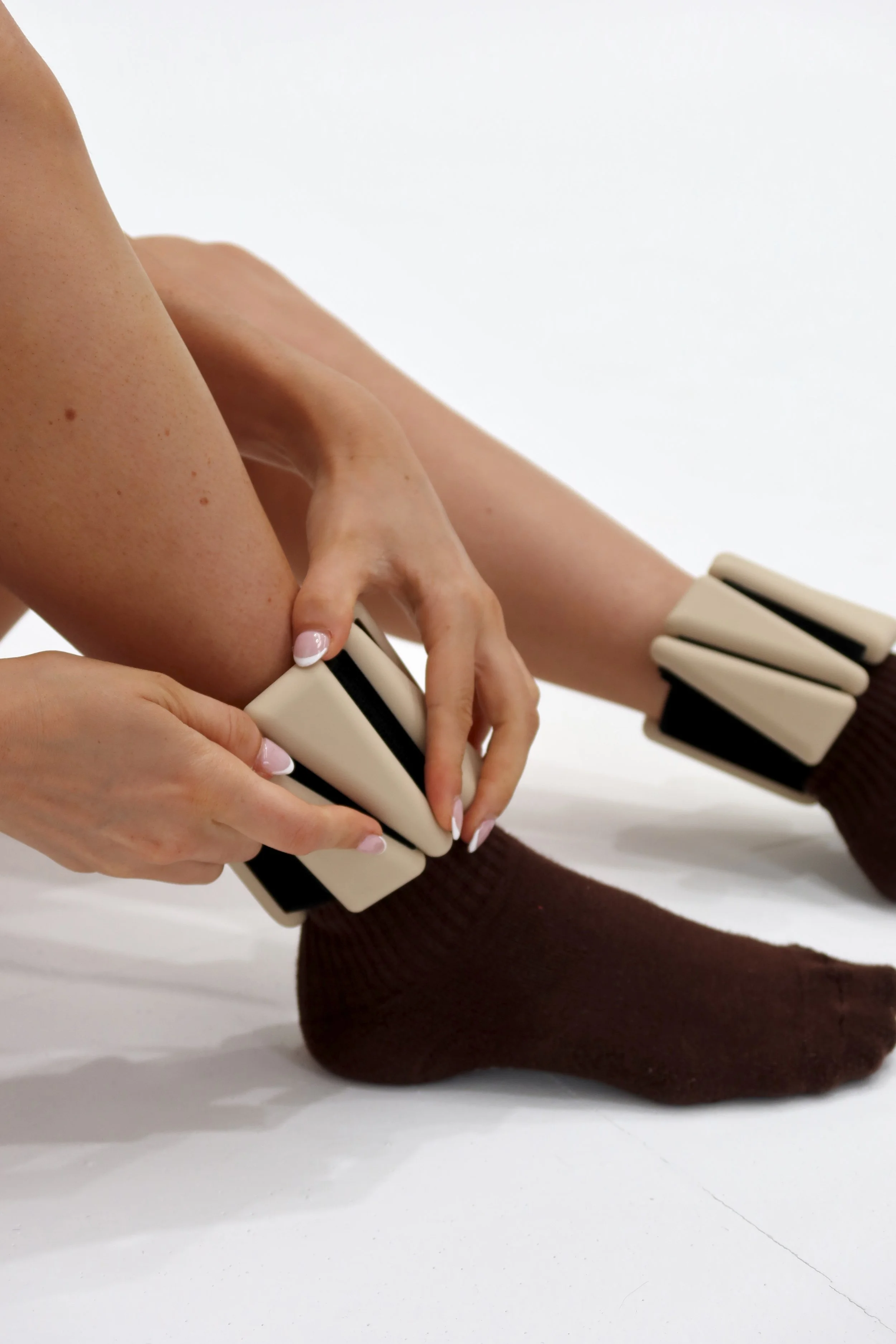 Person wearing brown socks with ankle weights wrapped around their ankles, against a white background.