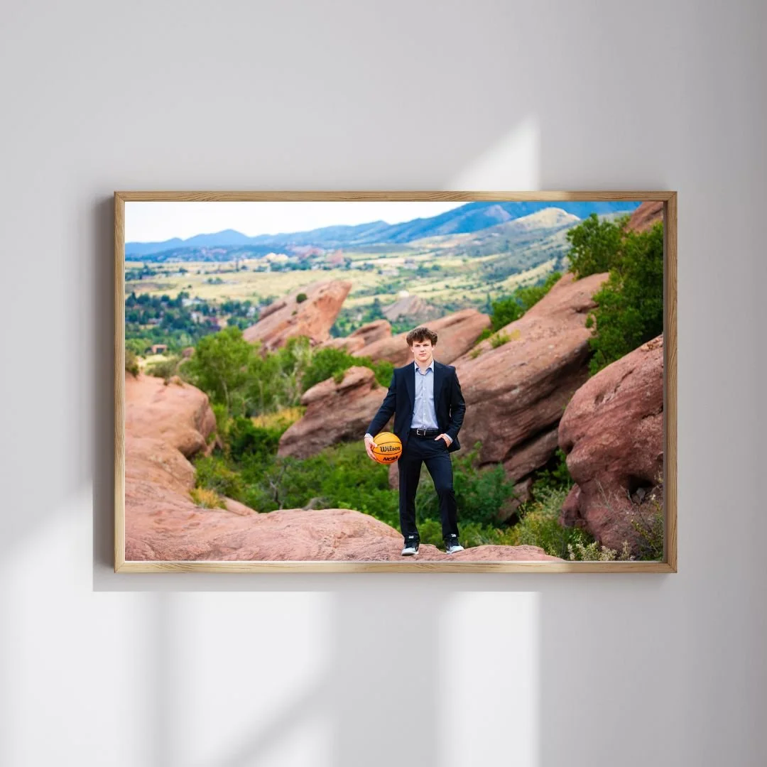 A young man in a suit standing on rocks in a desert landscape, holding a basketball.