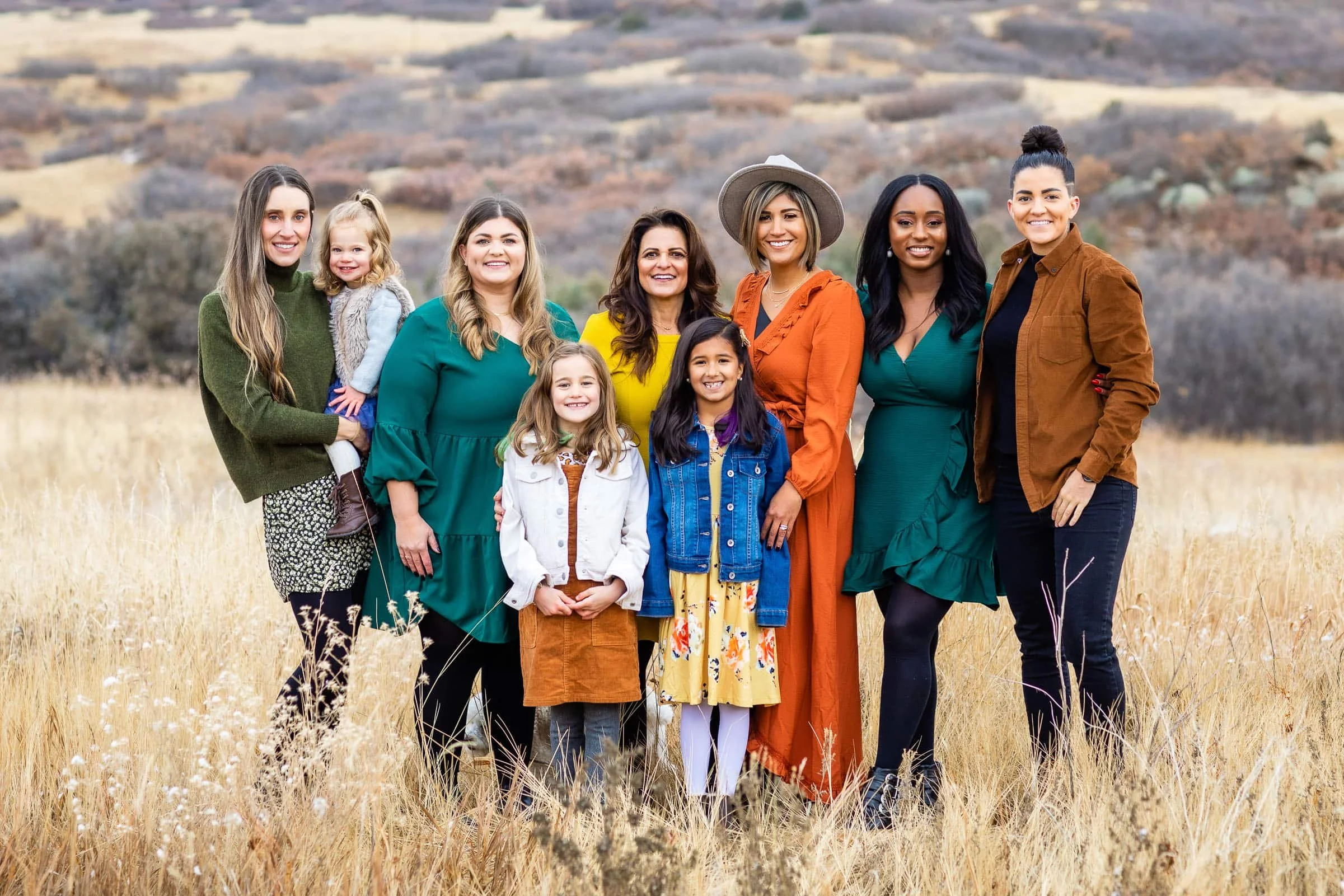 Group of women and children standing in a field with hills in the background, smiling at the camera.