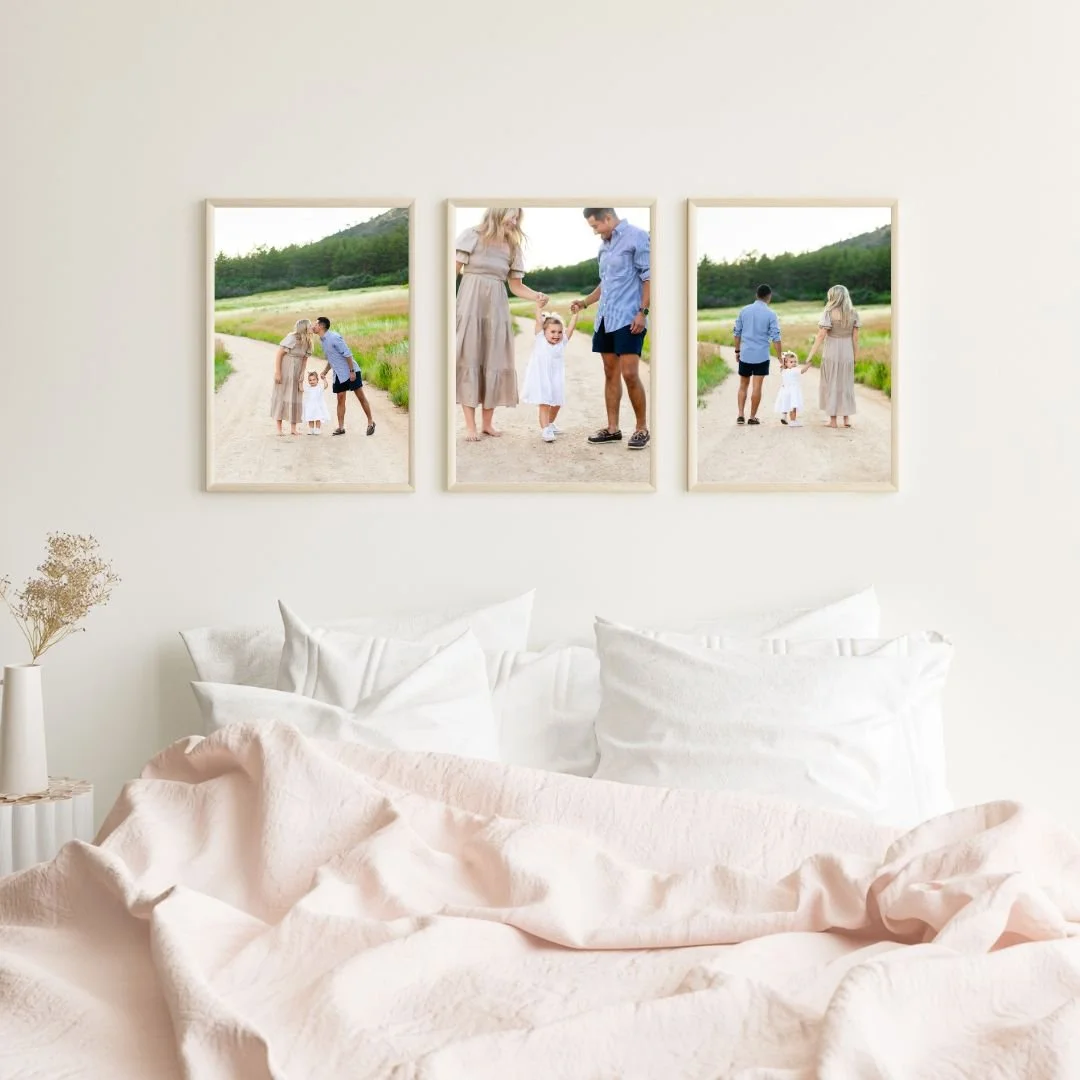 Three framed family photos hanging above a bed with white pillows and light pink bedding in a cozy bedroom.