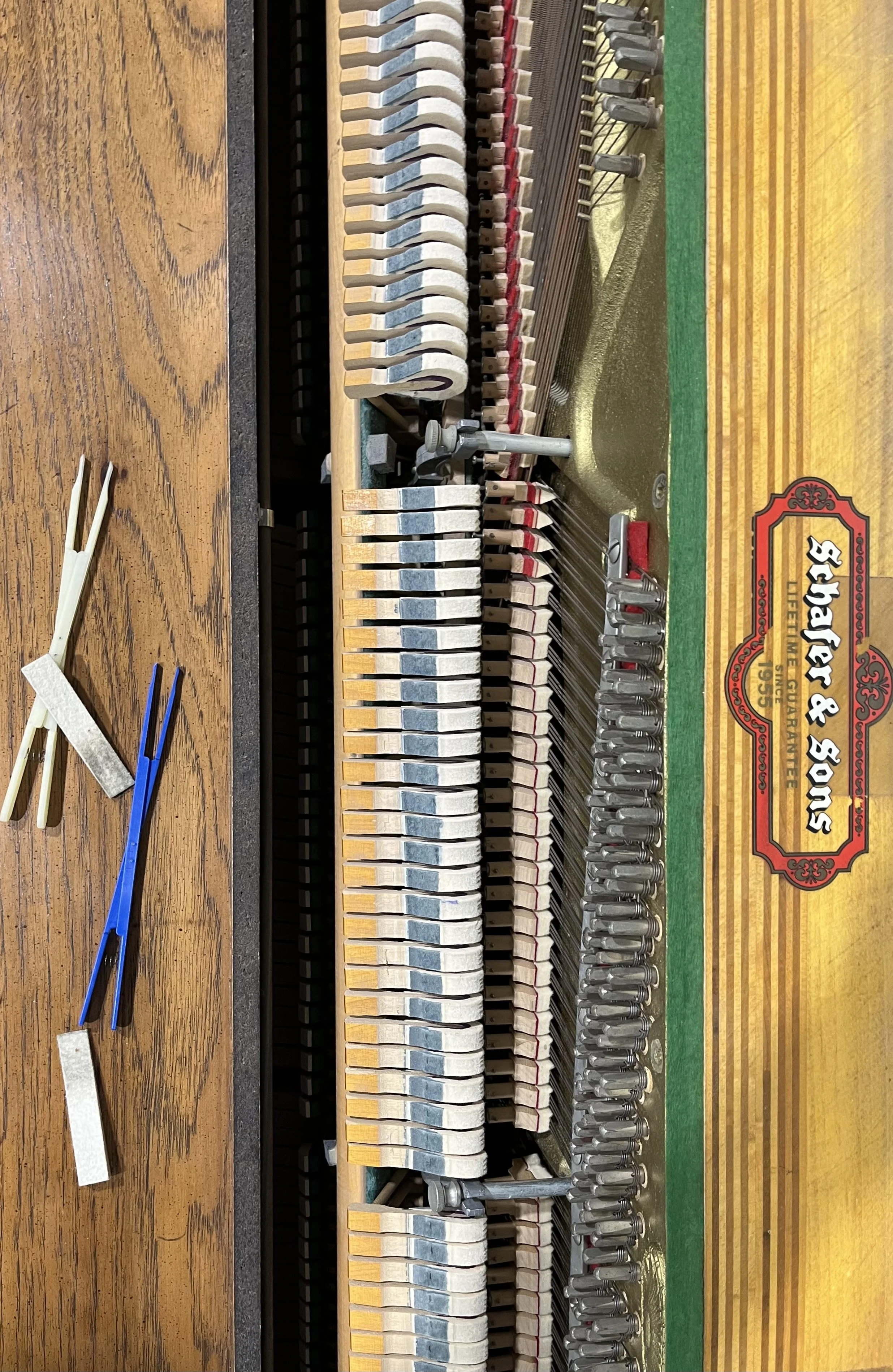 Close-up view of the internal mechanism of a piano, showing strings, hammers, and tuning pins. To the left are tuning tools, including tuning forks and a tuning hammer.