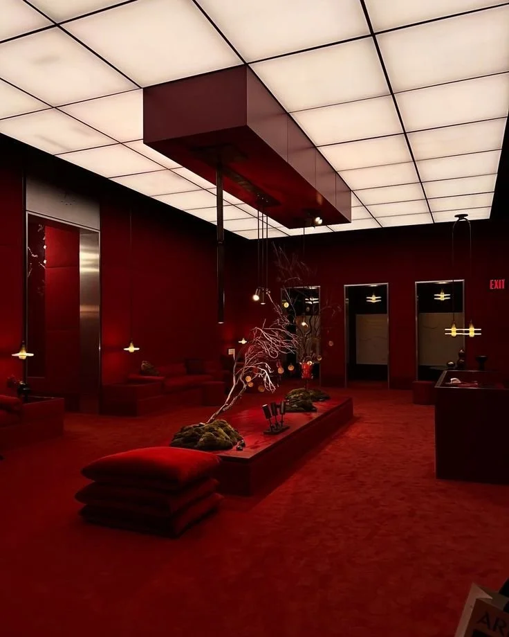 Interior of a modern room with red walls and a red carpet, featuring a central decorative setup with moss, a branch, and ornaments, illuminated by hanging pendant lights and overhead lighting.