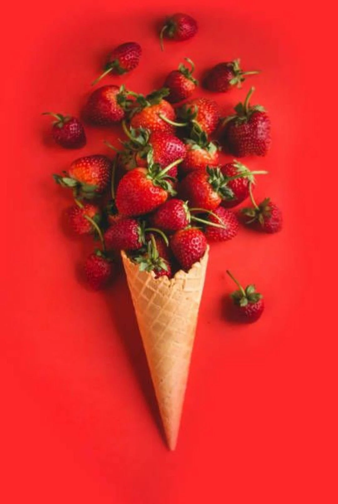 A waffle cone filled with fresh strawberries on a red background