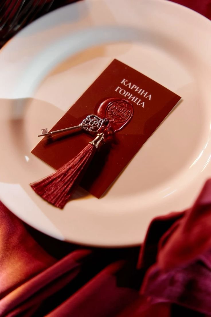 A white plate with a red business card featuring Cyrillic text, a decorative key with a tassel, and a wax seal.