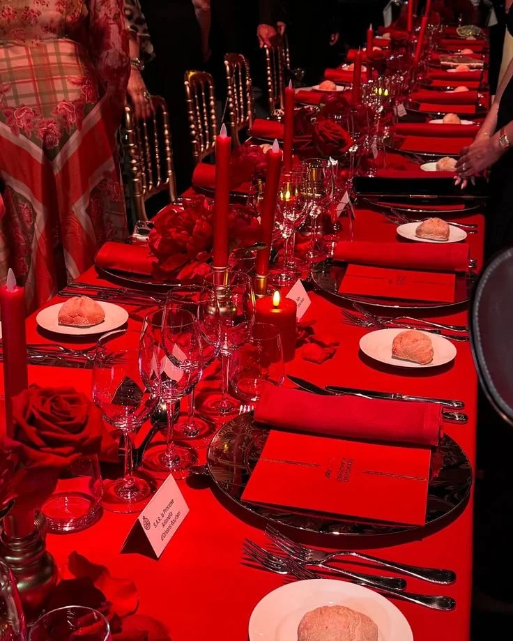 Elegant dining table decorated with red candles, roses, red tablecloth, and red napkins, set with glassware and plates, in a formal banquet setting.