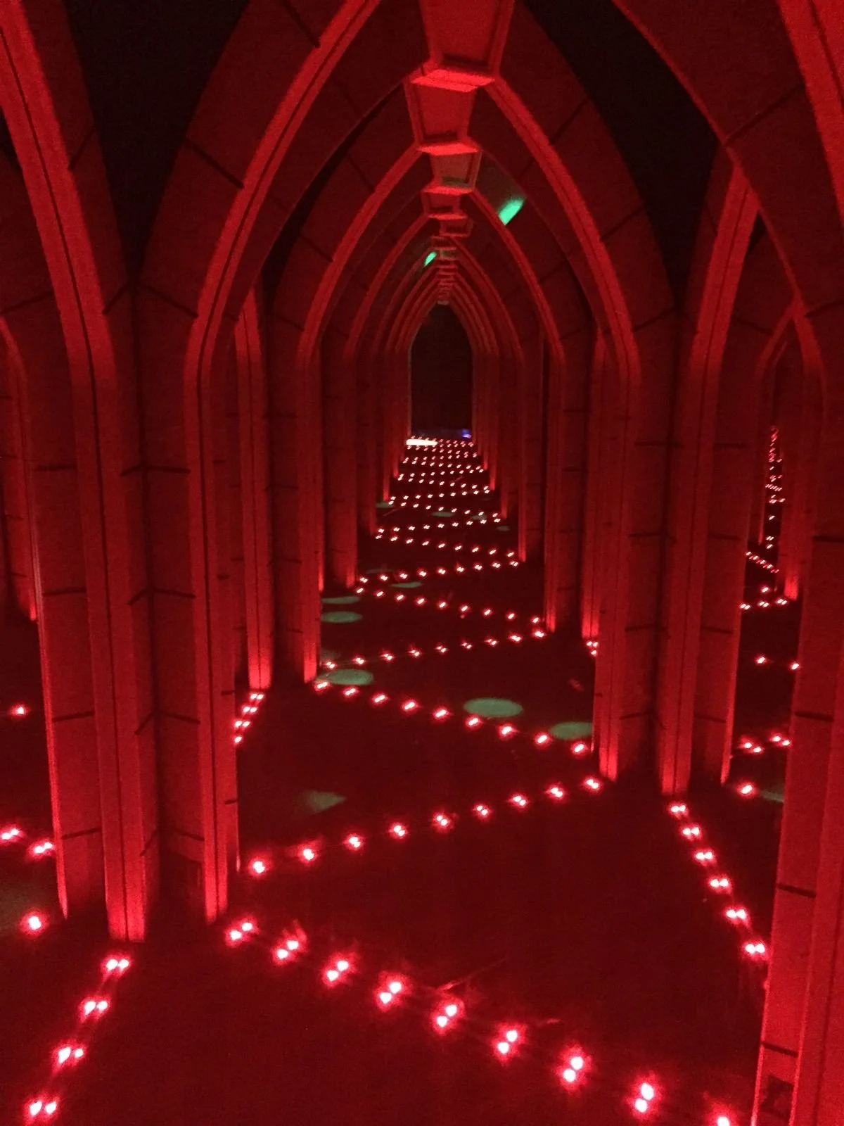 A tunnel with wooden arches illuminated by red lights, with pathways outlined by small red lights on the floor, creating an eerie, glowing effect.
