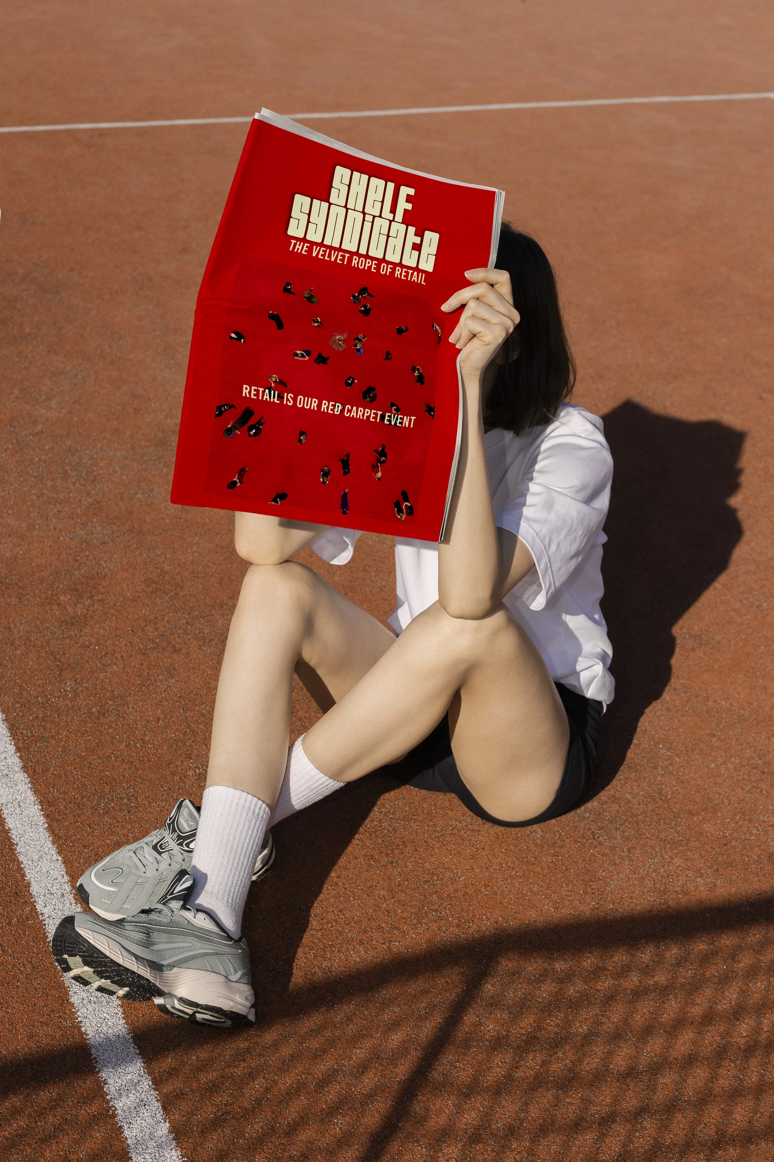 Person sitting on a sports track holding a large red magazine titled 'Shelf Synticate' with the subtitle 'The Velvet Rope of Retail' and a tagline 'Retail is Our Red Carpet Event'.