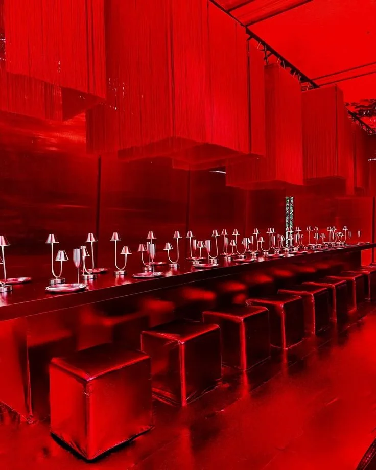 Red-themed dining area with a long bar counter, multiple champagne glasses, candleholders, and square stools in a luxurious setting.