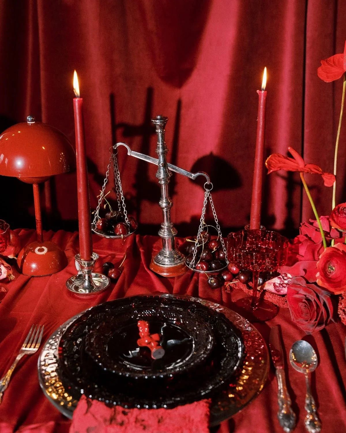 A table set for a romantic dinner with red candles, cherries, and floral decorations against a red backdrop.