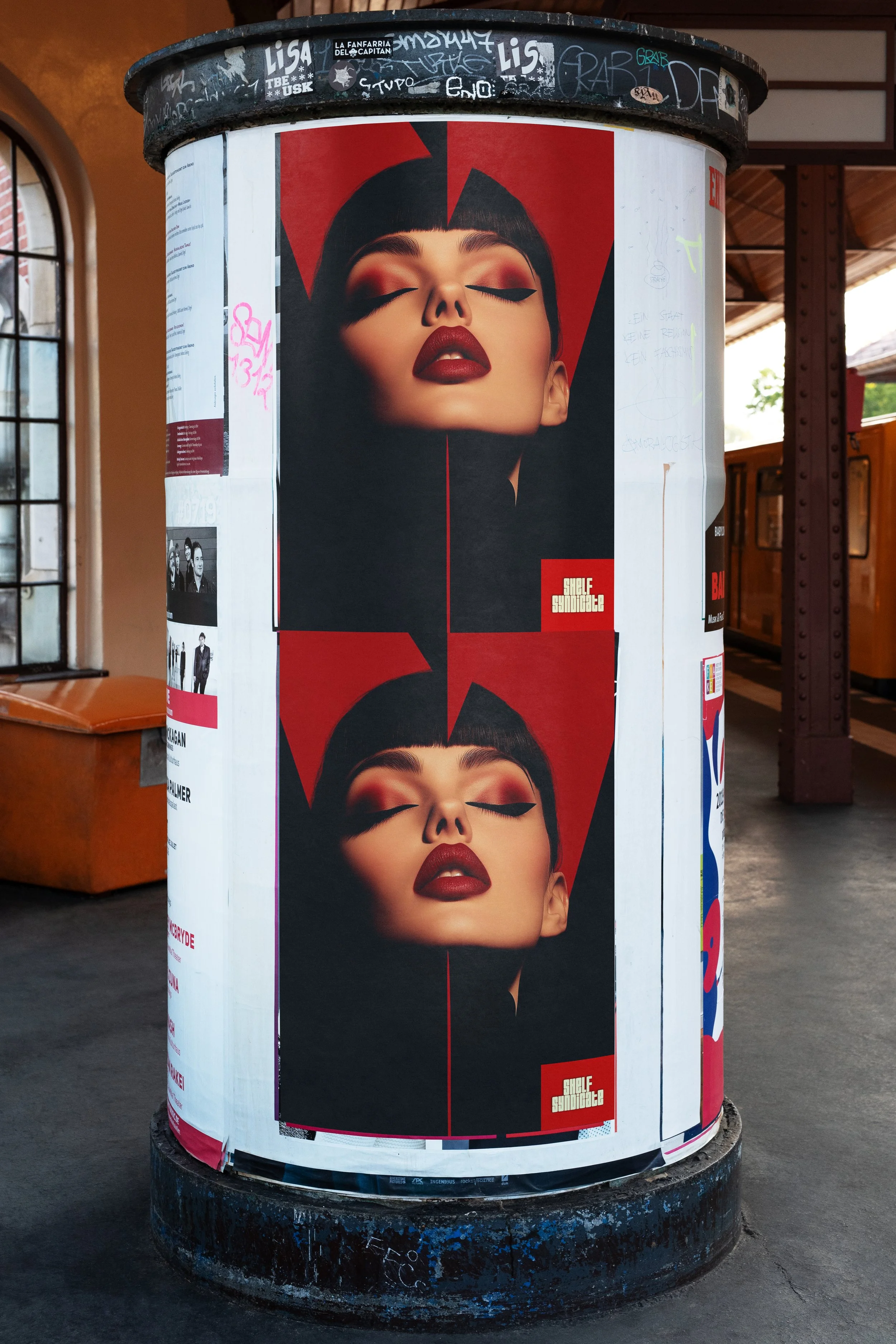 Poster on a cylindrical structure showing a woman with bold makeup and dark hair, with her eyes closed and head slightly tilted backwards. The poster features a red and black design with a logo that says "SUBLE SAMSOTAC".