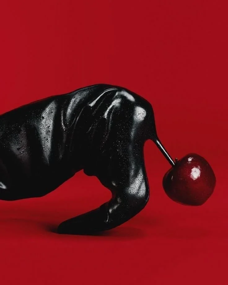 A black hand sculpture holding a cherry by its stem against a red background.