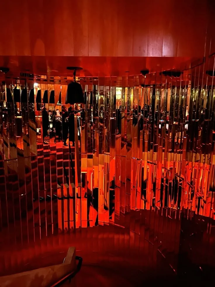 Interior of a modern, stylish space with reflective, metallic orange and red decor and hanging lights.