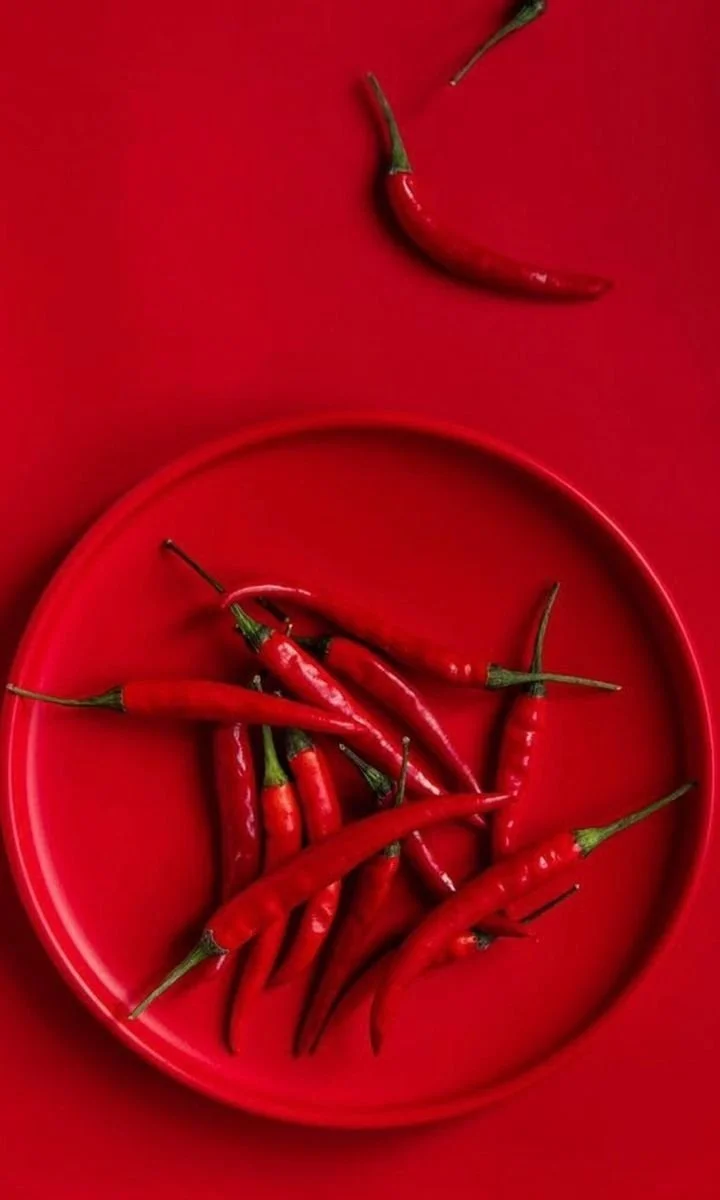 A red plate filled with red chili peppers on a red background.