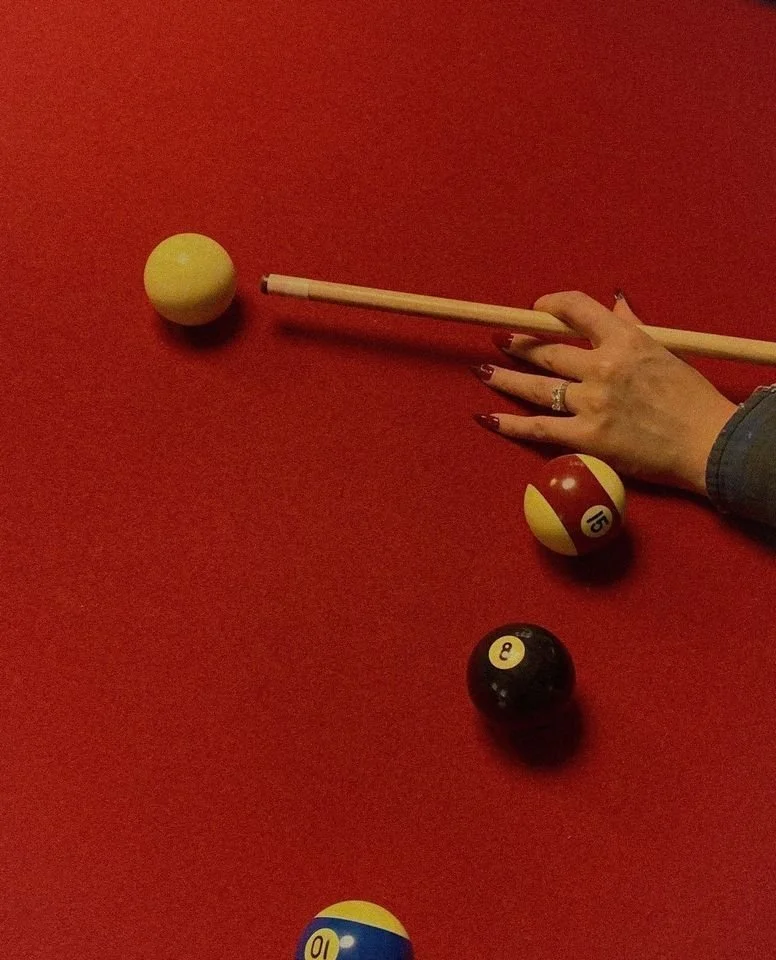 A person playing pool, holding a cue stick, on a red felt table with three pool balls near their hand.