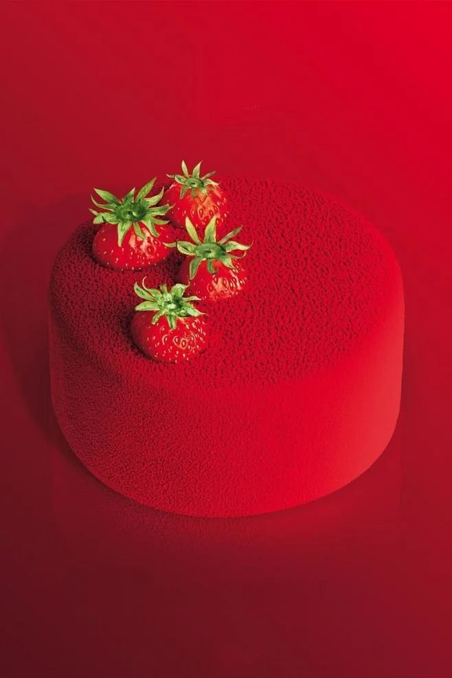 A large, red, textured object resembling a tomato with four smaller strawberries on top, set against a red background.