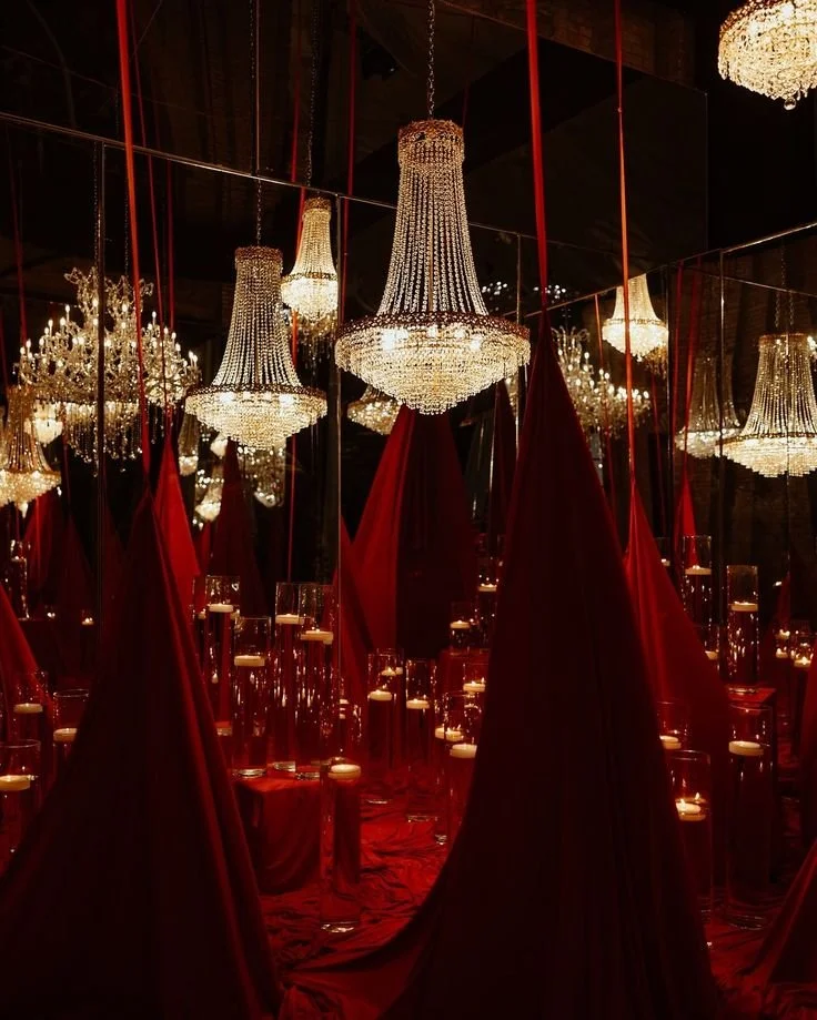 A room decorated with red curtains, multiple crystal chandeliers, and tall glass candle holders with lit candles, creating an elegant and luxurious atmosphere.