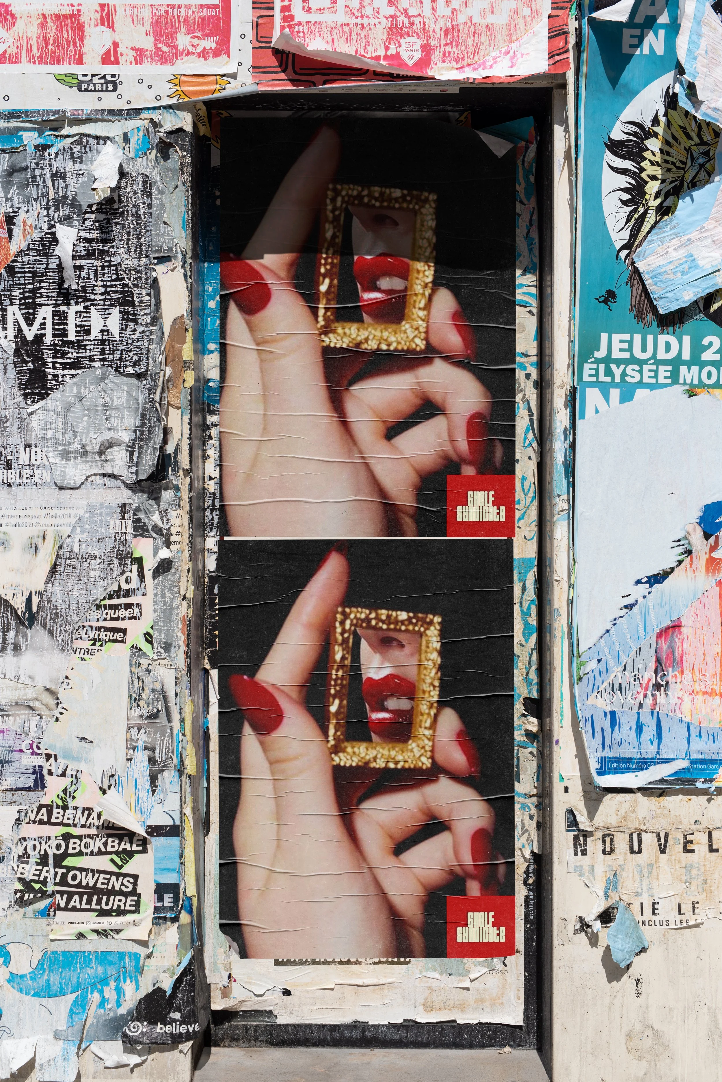 Street poster featuring a close-up of a hand with red nail polish holding a small, ornate gold picture frame. Inside the frame is a reflection of a woman’s lips with red lipstick and a partially visible nose. The poster appears to be part of a collage of torn, layered flyers and advertisements.