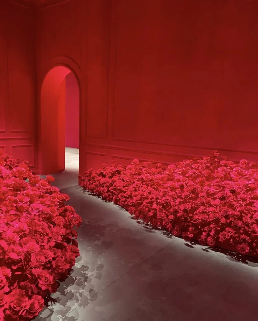 A hallway with red walls and pink flowers lining both sides of the walkway leading to an open door.