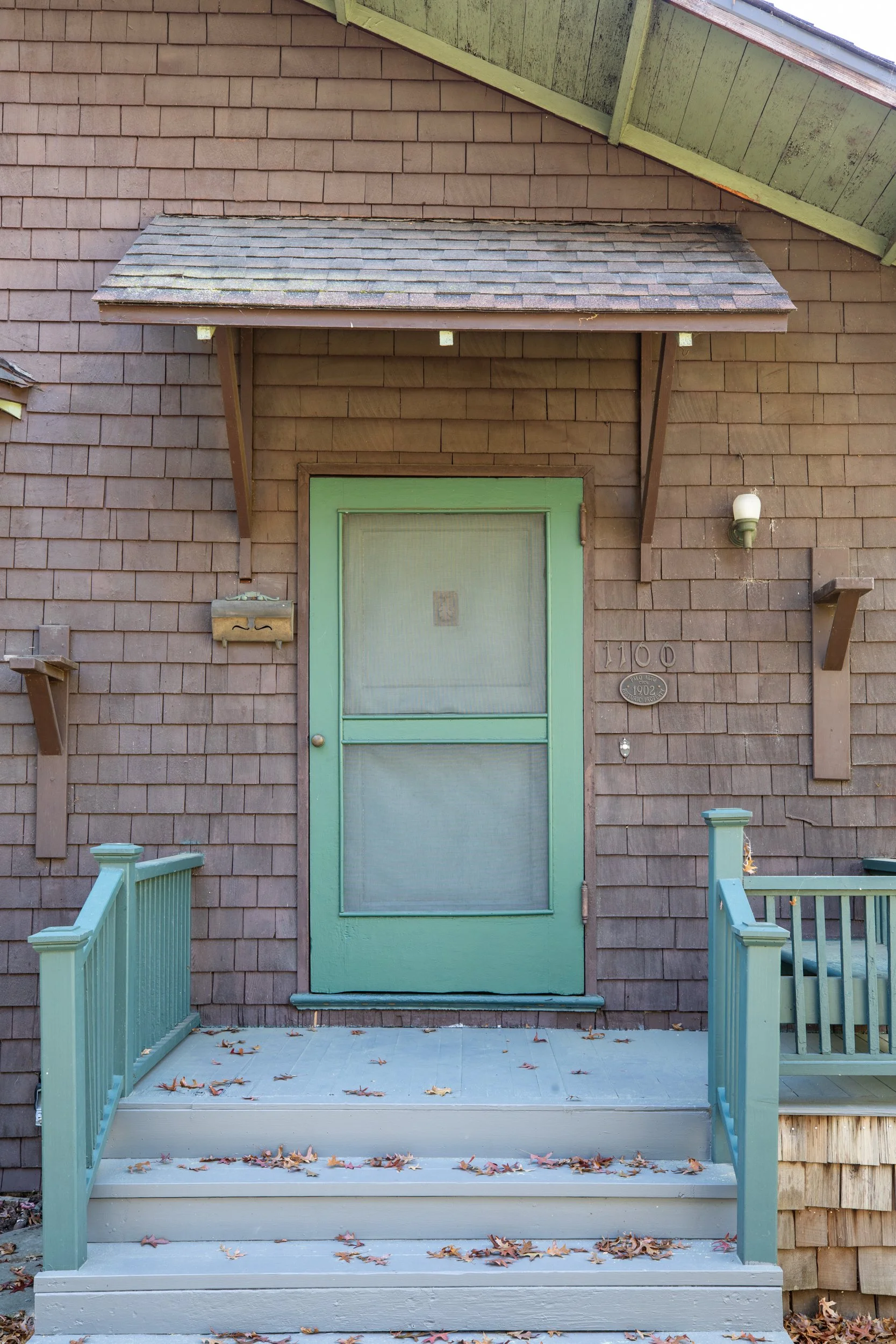 Front entrance of a house with a green door, small porch with stairs, and brown wooden siding.