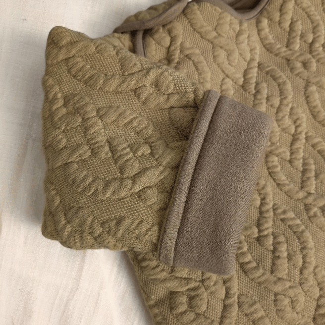 温かみのあるケーブル編みニット素材（ベージュ）。裏地はオーガニックコットンで赤ちゃんの肌を優しく包みます。
