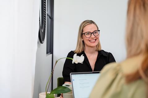 A woman with glasses smiling during a conversation in an office setting.