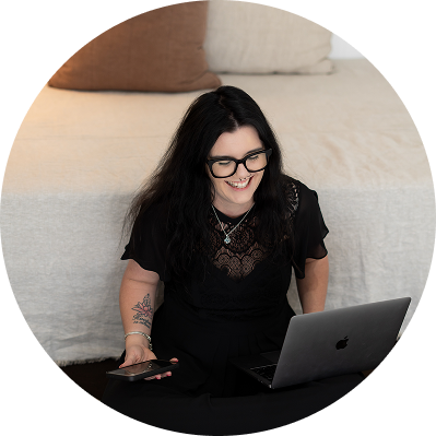 Woman with long dark hair and glasses smiling while working on a laptop at a desk.