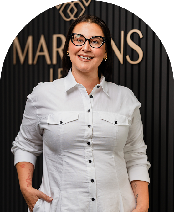 A smiling woman with glasses and earrings, wearing a white button-up shirt with rolled-up sleeves, standing in front of a black background with gold text and logo.