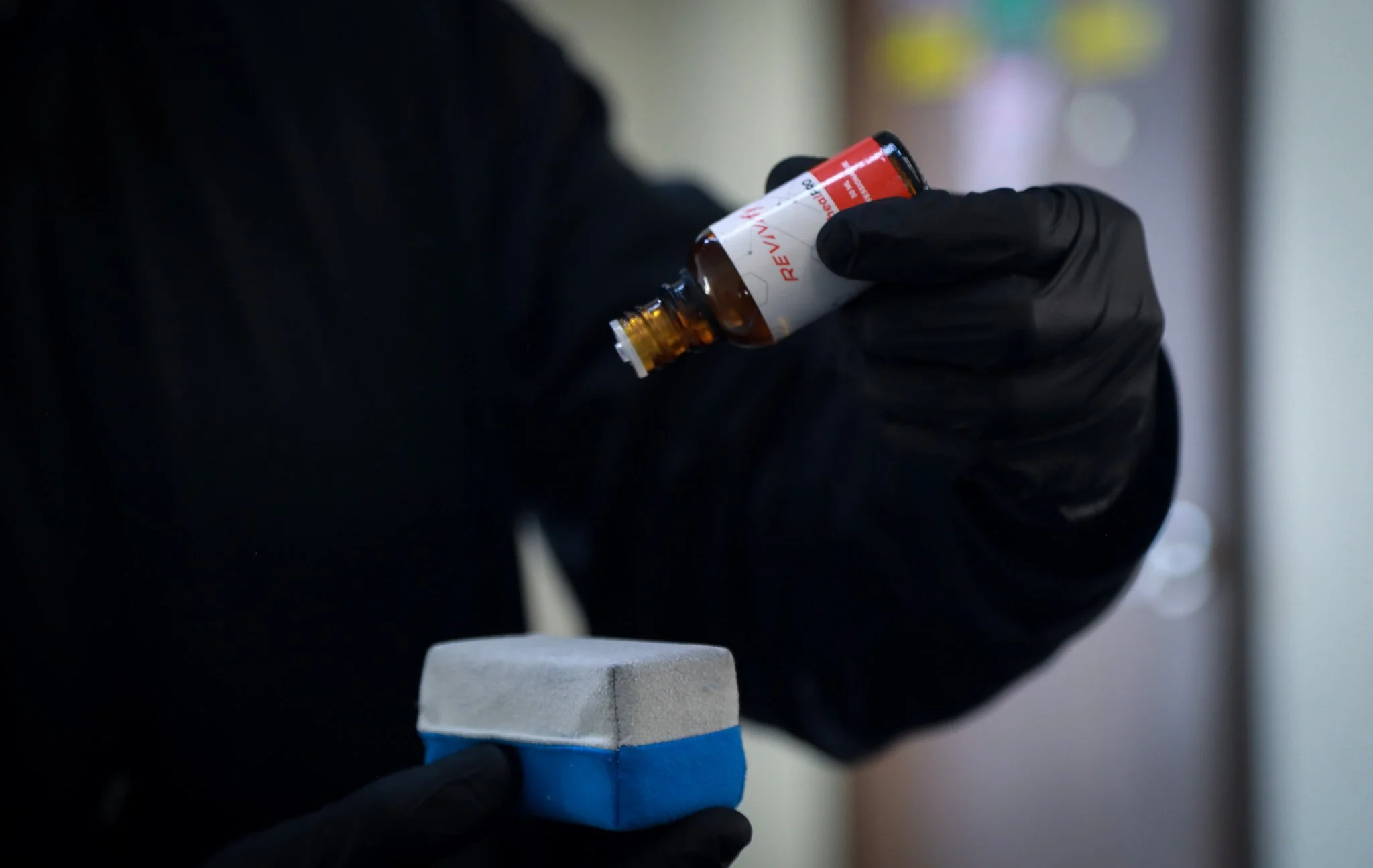 Person wearing black gloves holding a small bottle of medical substance and a cleaning sponge.