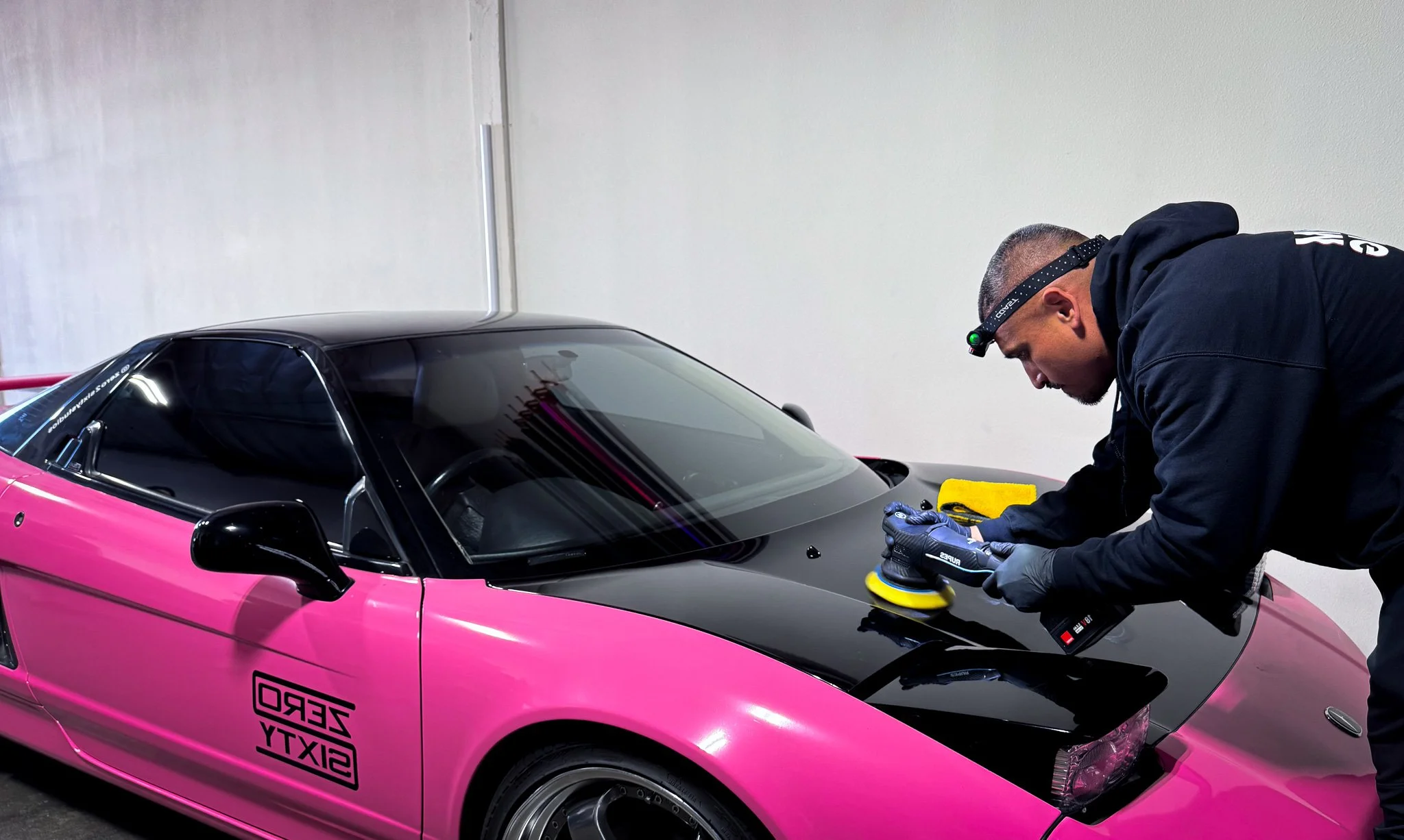 A person polishing a pink and black sports car in an indoor garage.
