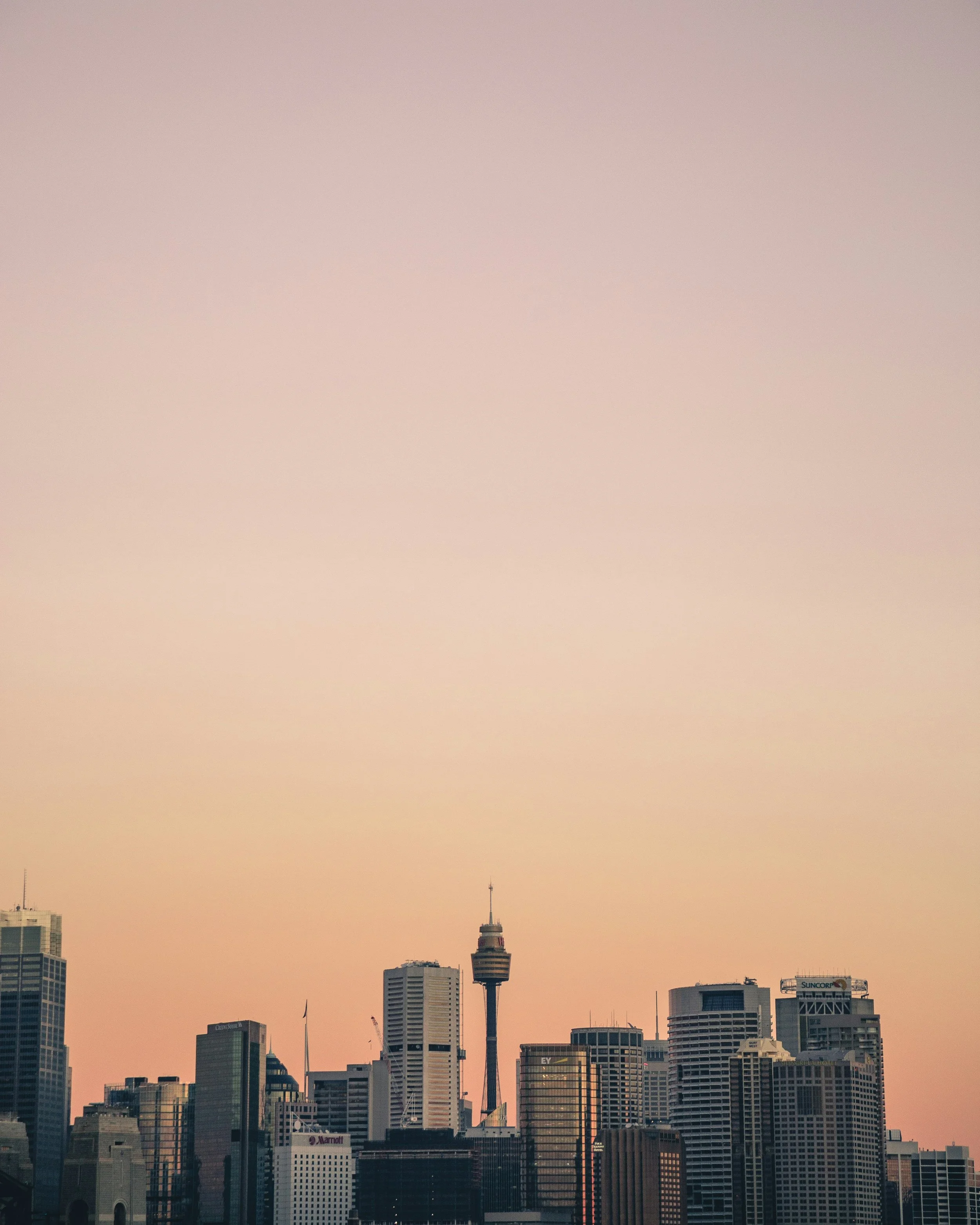 Sydney, Australia skyline of a city with skyscrapers and a tall communication tower under a pastel-colored sky.
