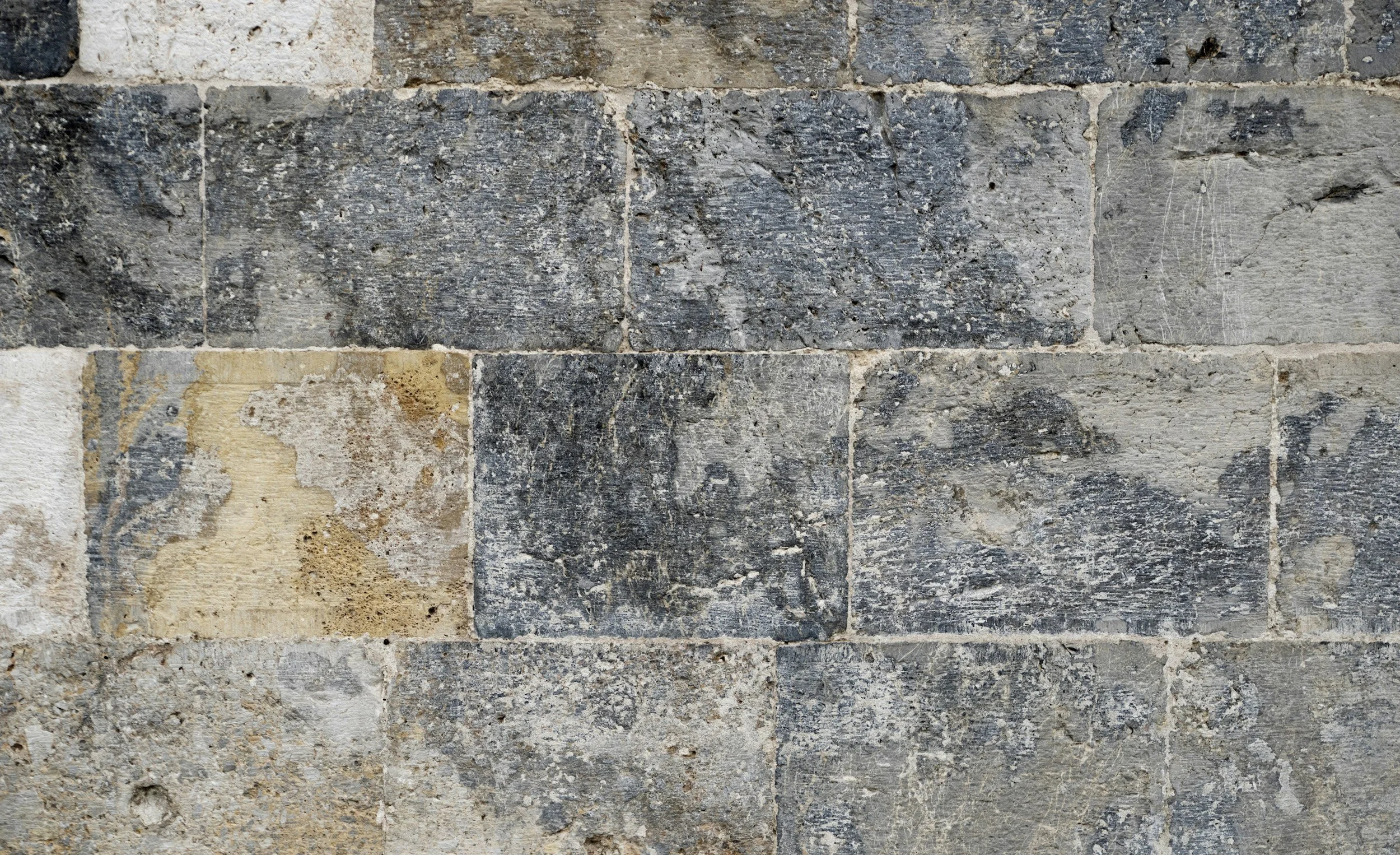 Close-up of an old stone brick wall with various shades of gray and beige, showing weathered and textured surfaces.