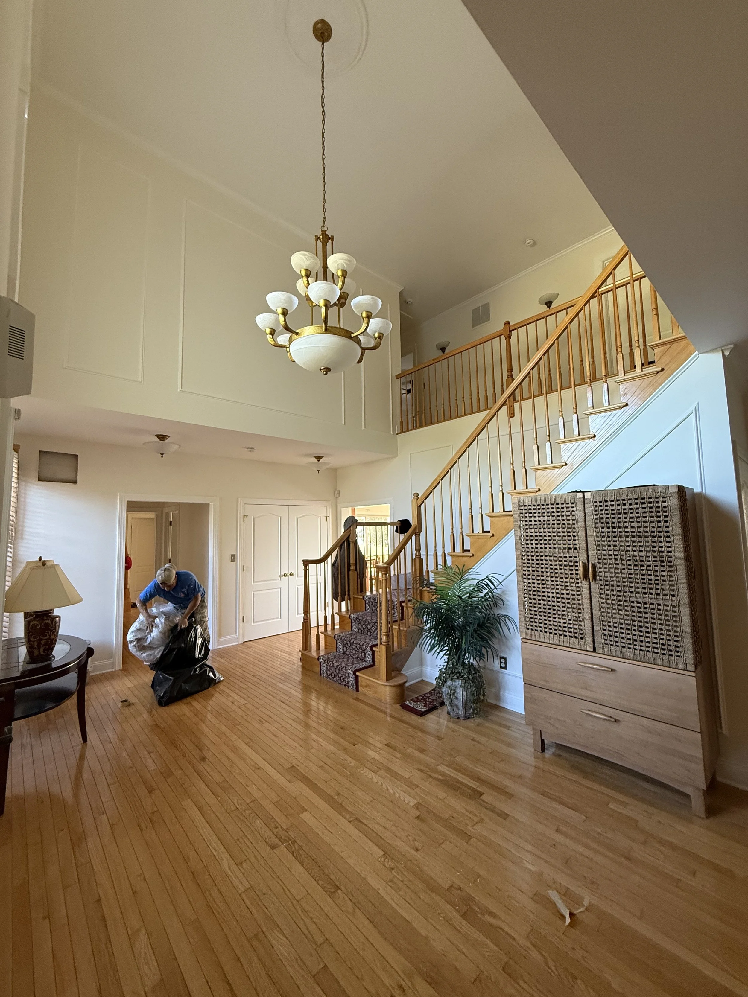 Interior view of a house with wooden floors, staircase, chandelier, a person with a white hair practicing, and a cabinet.