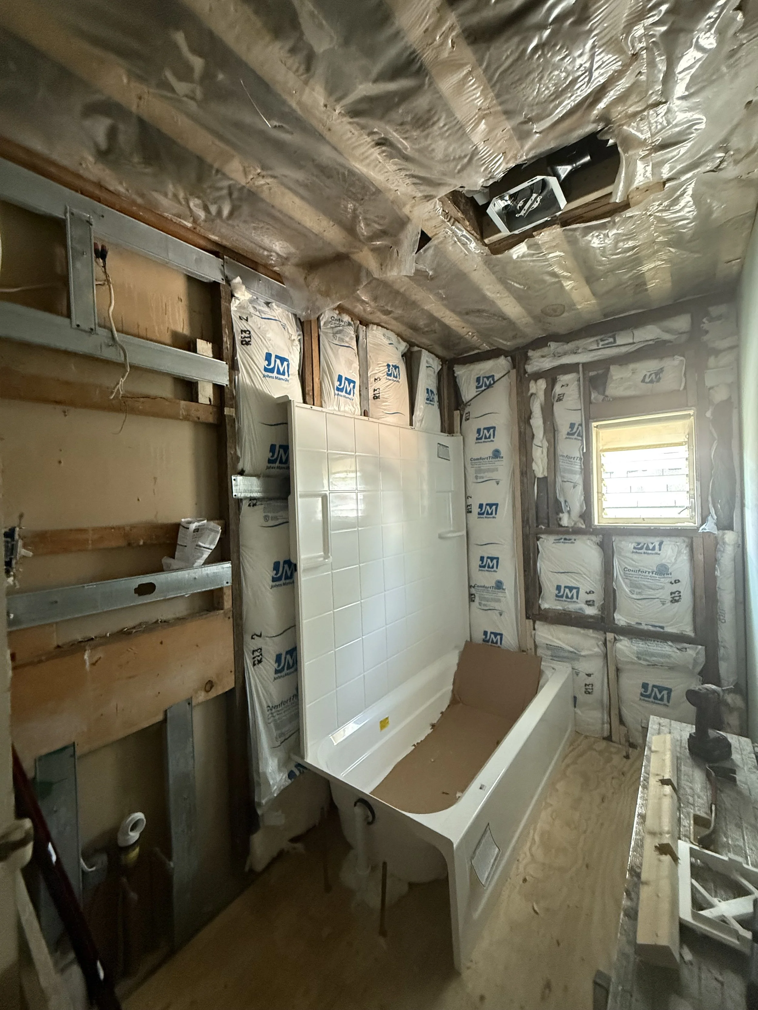 Bathroom under construction with a bathtub, insulation, and drywall framing.